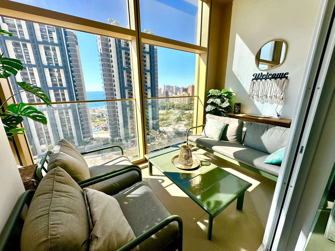 Salon apartamentu Gold & Gris z fotelami przy przeszklonej ścianie, widok na wieżowce Benidorm i morze